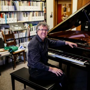 pianist Corey Hamm posing at the piano in his office
